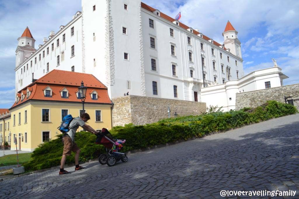 Pushing a stroller up the cobbled approach beside Bratislava Castle.