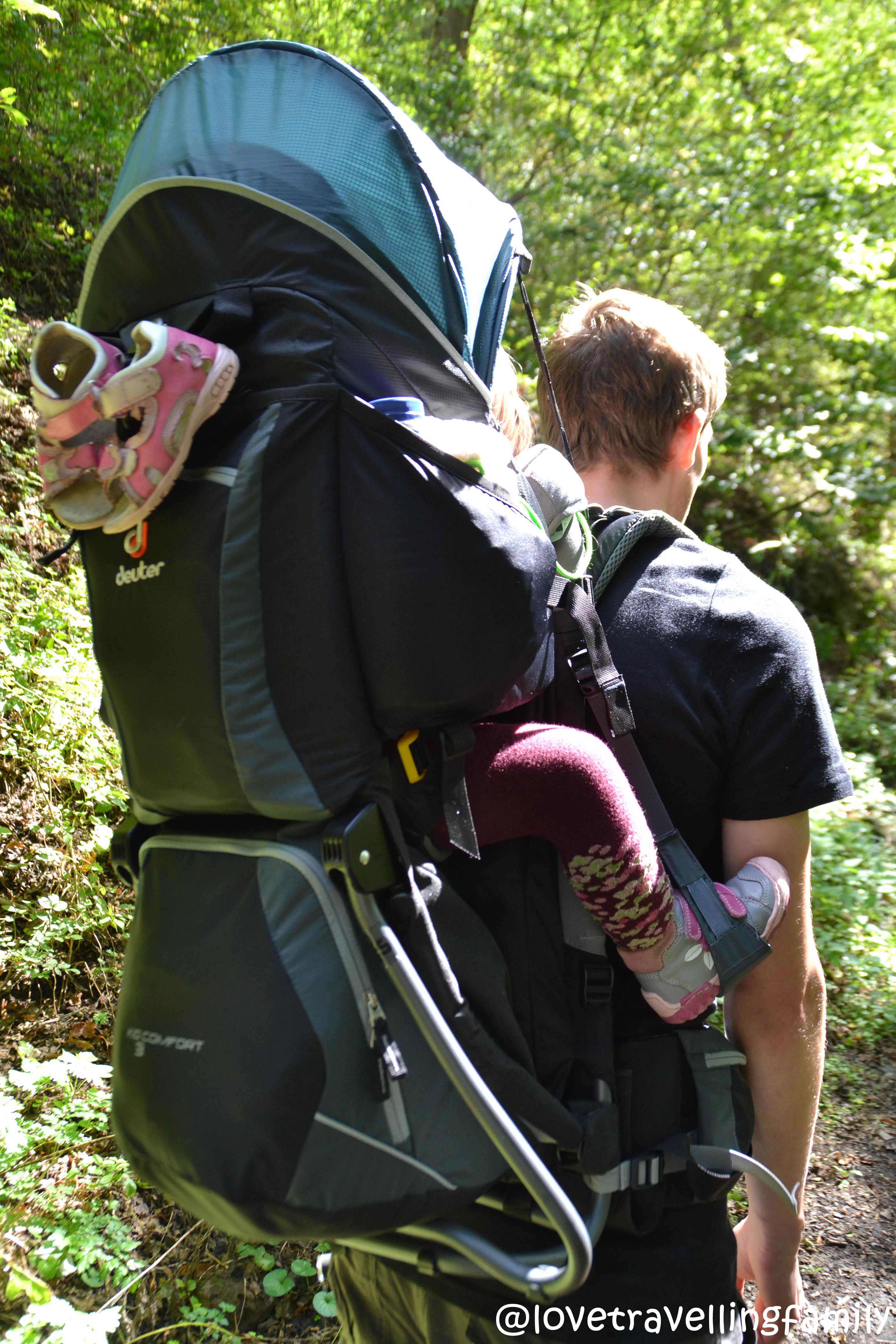 A father carries his daughter in a Deuter Kid Comfort 3 child carrier on a forest path.