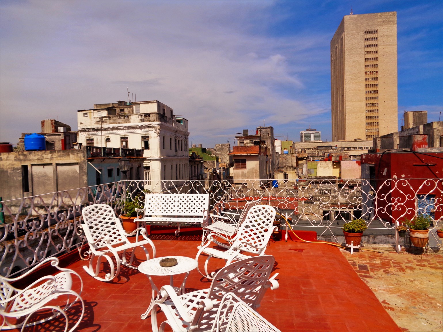 A red-tiled rooftop terrace with white wrought-iron rocking chairs above the rooftops of Centro Habana.