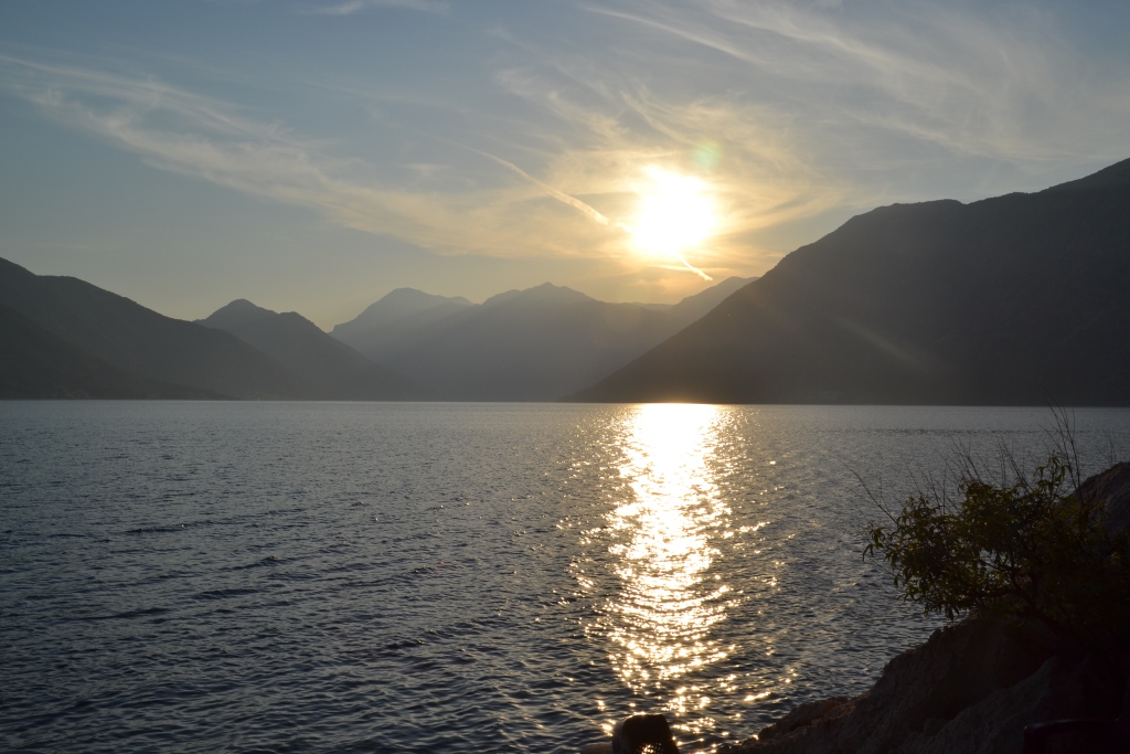 The sun setting over the calm water of the Bay of Kotor between dark mountains.