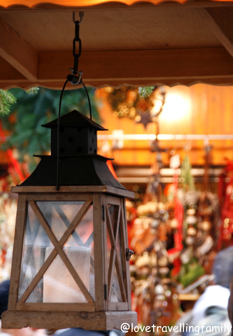 A hanging wooden lantern in front of a warmly lit Munich market stall.