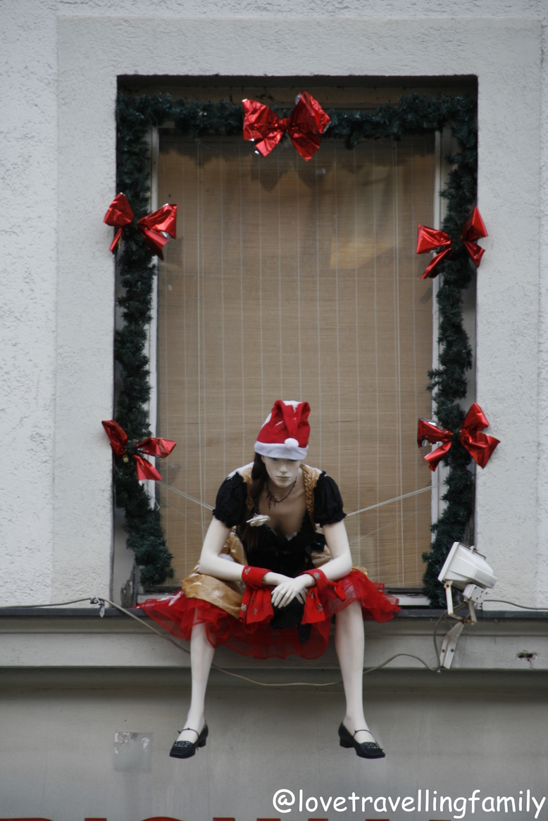 A seated mannequin in a Santa hat, framed by evergreen garlands and red bows.