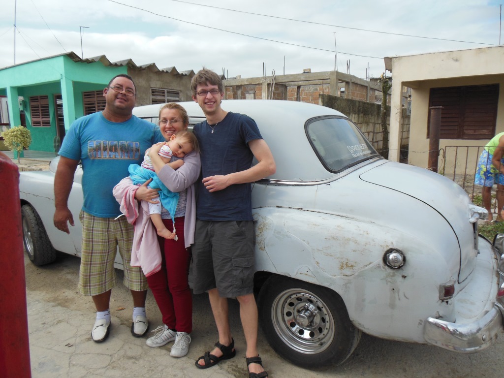 Our family and a driver beside an older white car during the journey to Playa Larga.